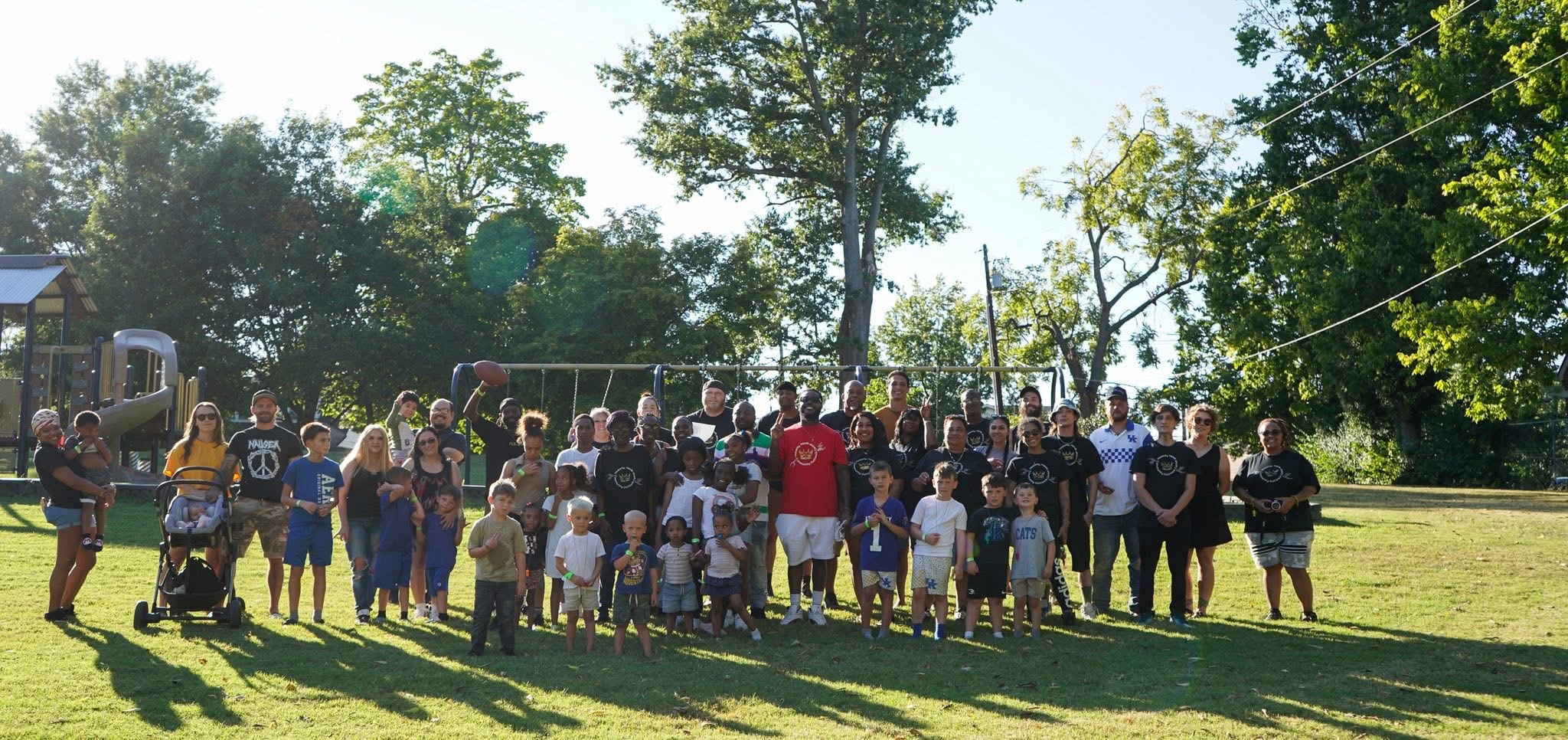 A community day in a park: neighbours and families gathered on the grass in front of the playground, with the TTL Operations crew in matching shirts among them.