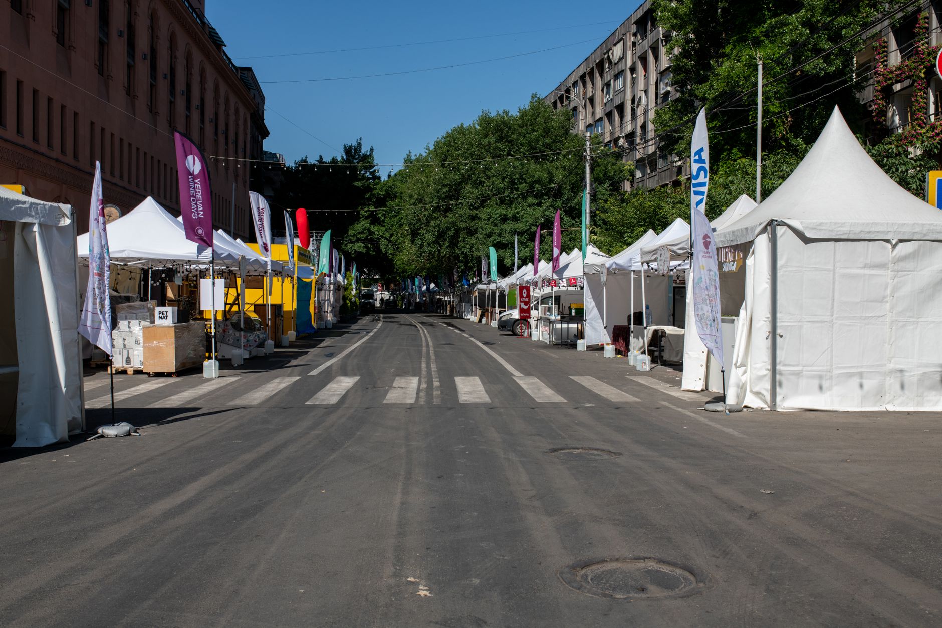 A street market before it opens: canopies up on both sides, flags strung overhead, and nobody on the road yet.